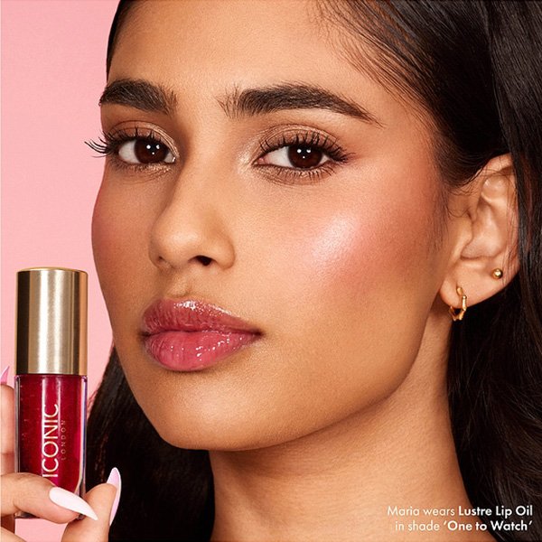 Lip Oil ICONIC LONDON Lustre One To Watch sheer red glossy lips with model holding gold-capped tube